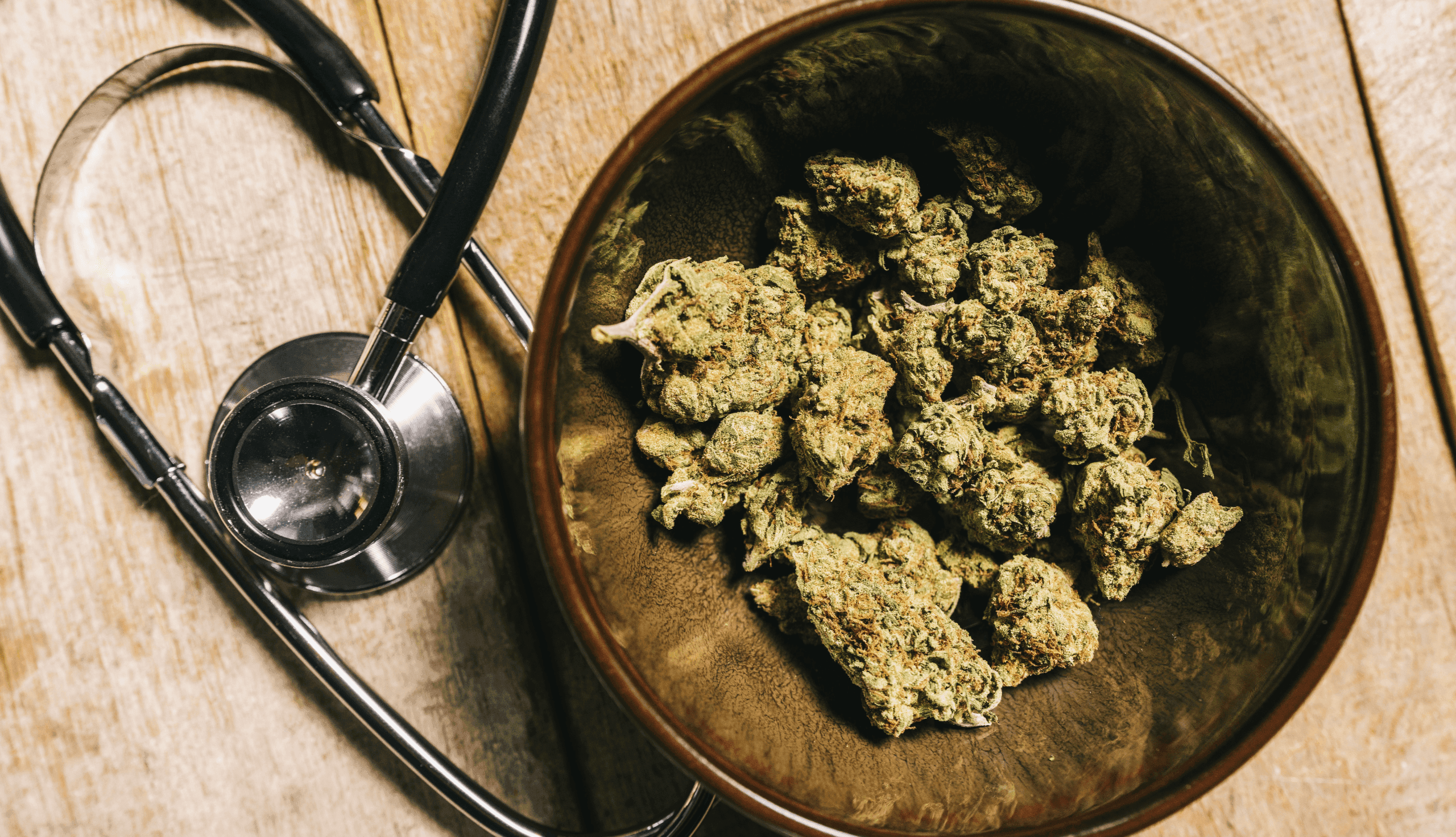 Schüssel mit medizinischem Cannabis und Stethoskop auf Holzoberfläche.